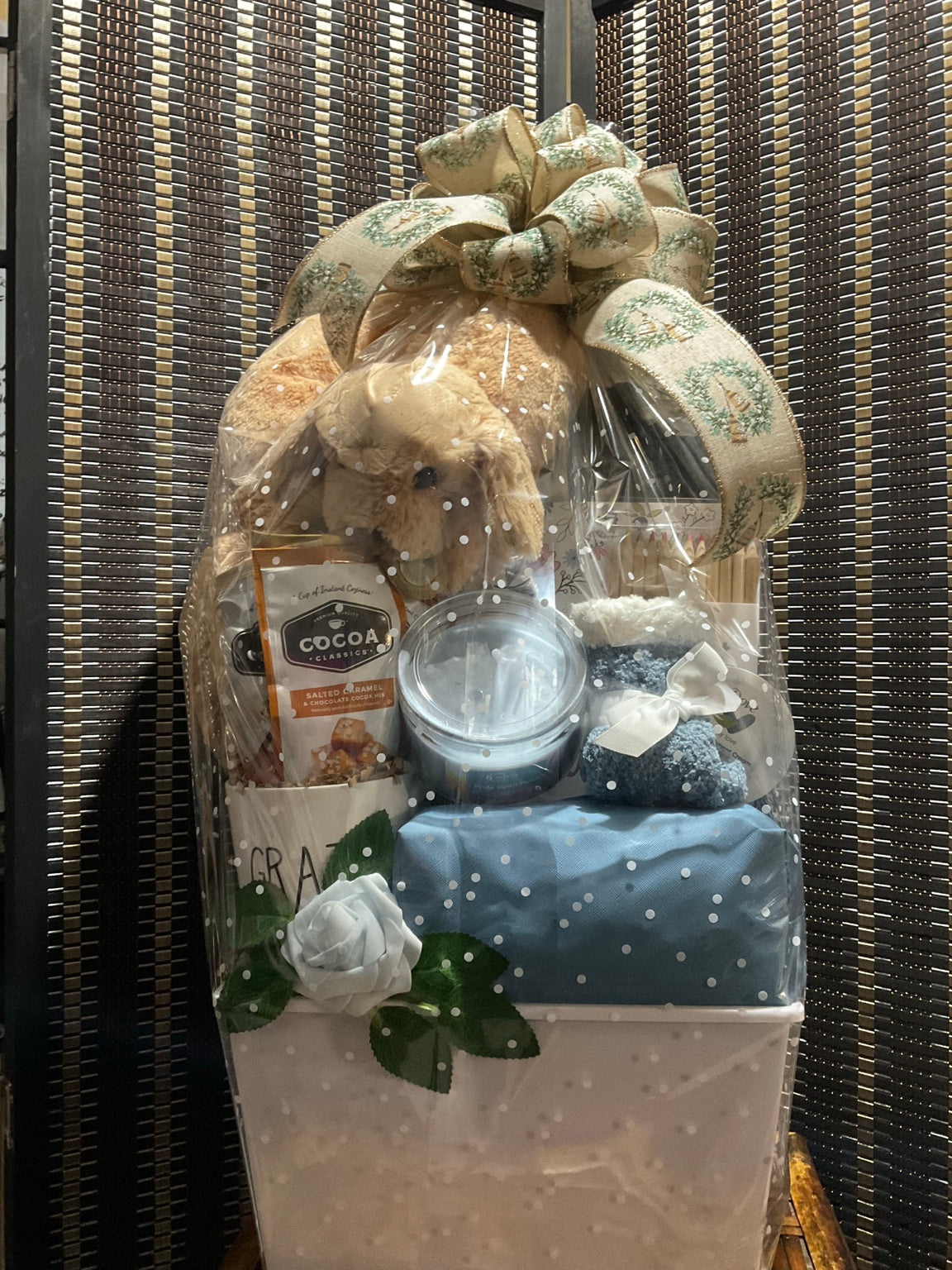 Wrapped comfort and creativity gift with plush dog, blanket, art supplies, candle, cocoa, flowers, and neutral bow