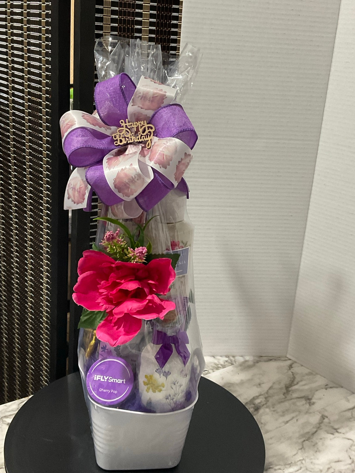 Petite purple and pink birthday gift arrangement with body care, prayer box, flowers, and layered birthday bow